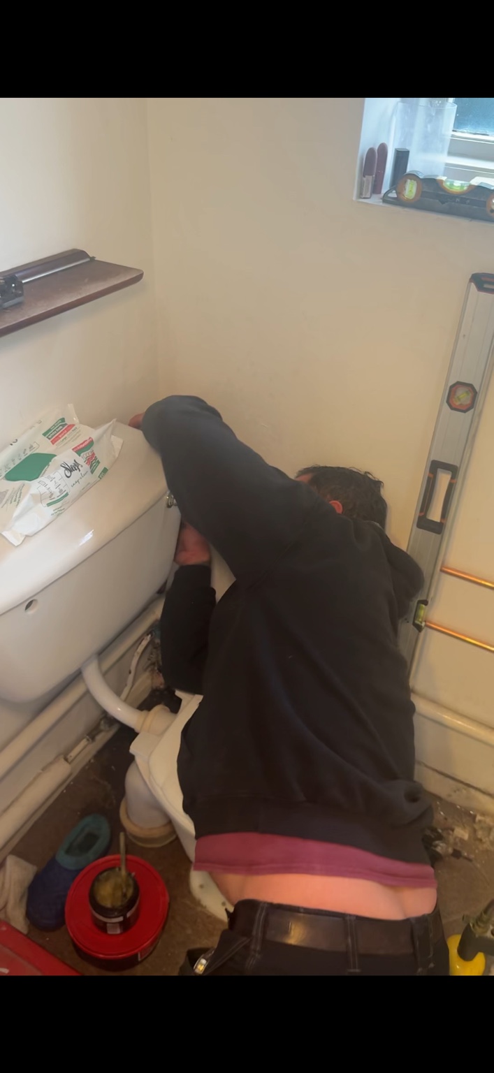 Plumber repairing toilet pipework in a customer bathroom